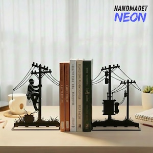 Puede incluir: Soportes para libros de metal negro con diseño de poste de electricidad. Uno muestra a un liniero subiendo un poste, el otro un transformador. El texto "HANDMADET NEON" está en la esquina superior derecha. Libros entre los topes.