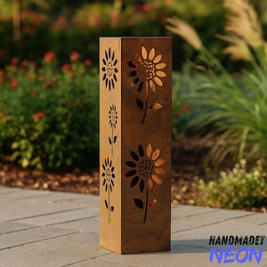 Può includere: Un'alta opera d'arte da giardino rettangolare in metallo marrone con disegni di girasoli ritagliati. Il pezzo ha un aspetto invecchiato e si trova su una superficie pavimentata. Il testo "HANDMADET NEON" è visibile in basso a destra.