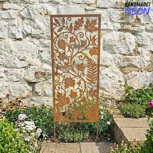 May include: A rectangular, rust-coloured metal garden screen featuring a cut-out leaf and vine design. The screen is supported by two stakes and is set in a garden bed with various plants and flowers. The text "HANDMADET NEON" is visible in the upper right corner.