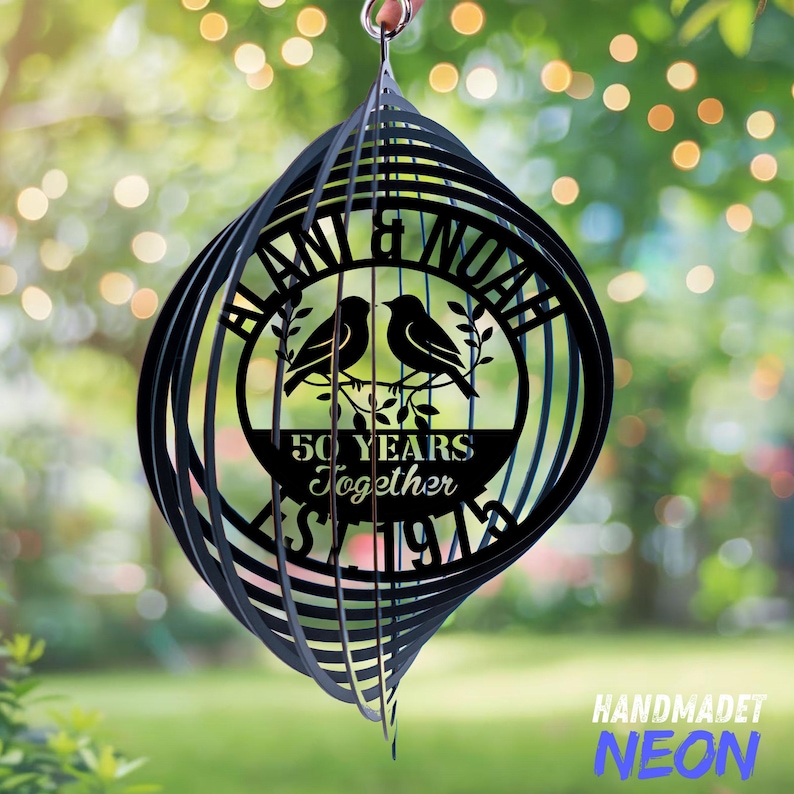 May include: Black metal wind spinner with a spiral design. The center features a circular design with two birds, the names "Blani & Noah", and the text "50 Years Together Since 1974". The bottom right corner has the text "HANDMADET NEON".