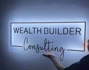 May include: A white illuminated sign with a black border and the text "WEALTH BUILDER Consulting" in black lettering.