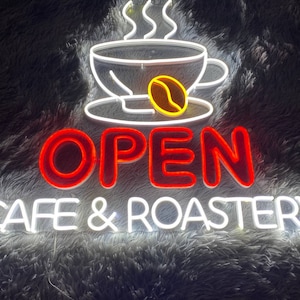 May include: A neon sign with a red "OPEN" sign and a white "CAFE & ROASTERY" sign. The sign features a white neon coffee cup with steam and a yellow coffee bean.