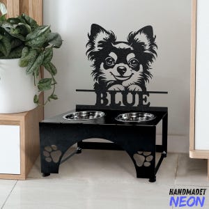 Könnte beinhalten: Schwarzer Metall-Hunde-Napfständer mit zwei Näpfen. Der Ständer zeigt eine Silhouette eines Chihuahuas mit dem Namen "BLUE" darunter. Der Ständer hat Pfotenabdrücke auf der Unterseite.