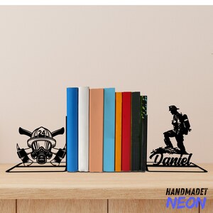 May include: Black metal bookends featuring a firefighter silhouette with the name "Daniel" and a firefighter helmet with crossed axes. The bookends are holding up a row of colorful books.