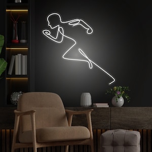 Puede incluir: Un letrero de neón blanco que representa a una persona corriendo en un estilo de arte de una sola línea. El letrero está montado en una pared negra sobre un sillón marrón y un otomano marrón oscuro.