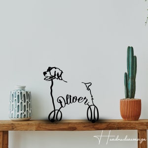 Könnte beinhalten: Schwarze Metallsilhouette eines Hundes mit dem Namen "Oliver" in Kursivschrift. Die Silhouette steht auf einem Holzregal mit einem Topf-Kaktus und einer dekorativen Vase.