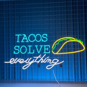 May include: Neon sign with the text "Tacos Solve Everything" in blue and white. A yellow neon taco with green filling is above the text.