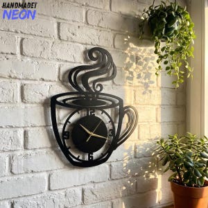 Peut inclure: Une horloge murale noire en forme de tasse à café avec de la vapeur s'élevant du sommet. Le cadran est circulaire avec des chiffres noirs et de fines aiguilles dorées. Le design présente une silhouette découpée de tasse avec une anse.