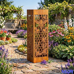May include: A tall, rectangular, rusted metal garden lantern with cut-out bee and honeycomb designs. The lantern stands on a brick pathway, surrounded by a vibrant garden with flowers and greenery. The lantern is a decorative outdoor accent.