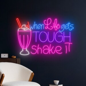 May include: Neon sign with a milkshake and the text "When life gets tough shake it". The sign is pink and blue.