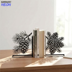 May include: A pair of black metal bookends featuring intricate laser-cut designs of pine cones and pine needles. The left bookend displays a single pine cone on a branch, while the right bookend shows a cluster of three pine cones on branches.