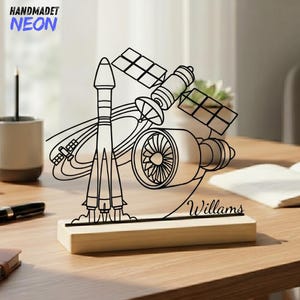 May include: A black line art neon sign featuring a rocket, satellite, and jet engine design. The sign is mounted on a light-colored wooden base with the name "Willams" inscribed. The top left corner has the text "HANDMADET NEON".