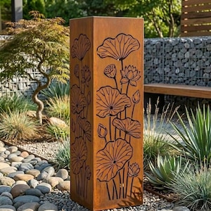 May include: A tall, rectangular, weathered metal garden sculpture with a lotus flower design. The sculpture is a rusty brown color and features cut-out lotus flowers and leaves. It stands in a garden setting with rocks and greenery.