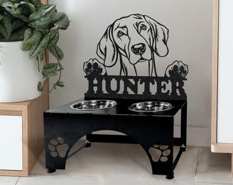 May include: Black metal dog bowl stand with two bowls. The stand features a cutout of a Weimaraner dog with the name "Hunter" above the bowls.