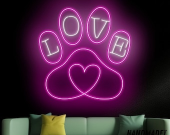 May include: Pink neon sign shaped like a paw print with the word "LOVE" spelled out around the paw print and a heart in the center. The sign is hanging on a wall behind a green couch.