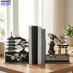 Puede incluir: Sujetalibros de metal negro con temática japonesa. Uno presenta una pagoda, una montaña y flores de cerezo. El otro representa una geisha con un paraguas, una puerta torii y grullas de origami. Los sujetalibros sostienen varios libros.