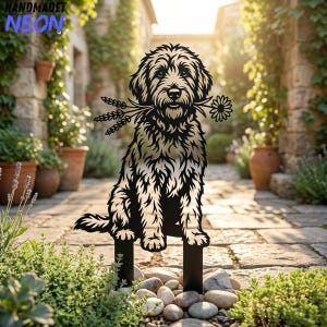 May include: A black metal garden stake featuring a cutout silhouette of a shaggy-haired dog sitting and holding a sprig of wheat and a daisy in its mouth. The design includes two vertical prongs at the base for insertion into the ground.