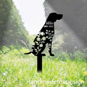 Op de afbeelding: Zwarte metalen silhouet van een hond met bloemmotieven, zittend op een paal. De naam van de hond "Milo" en de data "2010-2024" zijn gegraveerd in het silhouet.