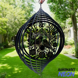 May include: Black metal wind spinner with a spiral design. The center features a birdhouse design with two birds, floral accents, and the names "KATE & JOHN" and "EST 2000". The words "HANDMADET NEON" are at the bottom.