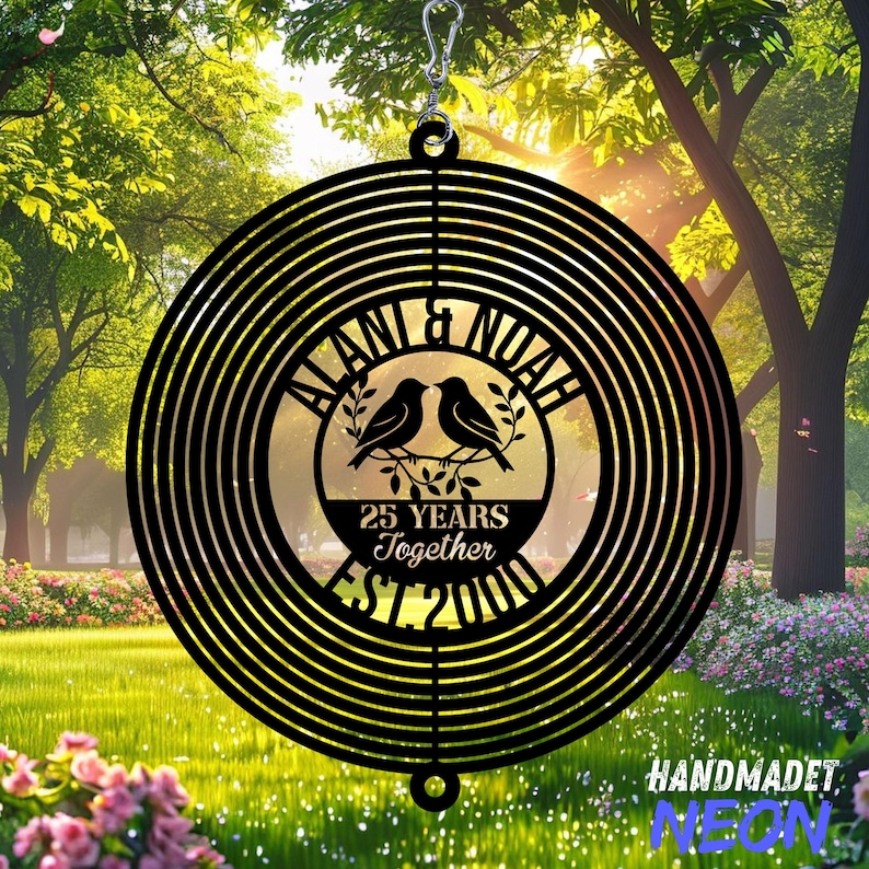 Pode incluir: Moinho de vento de metal preto com um design circular. O centro apresenta dois p&aacute;ssaros empoleirados num galho, com os nomes "ALANI & NOAH" e o texto "25 YEARS Together EST 2000". O moinho de vento &eacute; pendurado por um gancho prateado.