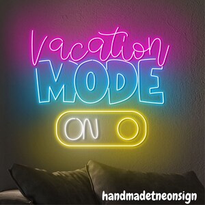 May include: Neon sign with the text "Vacation Mode On" in pink, blue, and yellow. The sign is on a wall with a couch in the foreground.