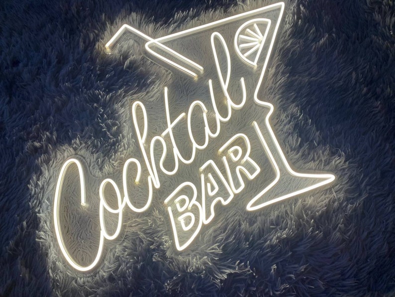 K&ouml;nnte beinhalten: Wei&szlig;es Neon-Schild mit den Worten "Cocktail Bar" und einem stilisierten Cocktailglas mit einer Zitronenscheibe.