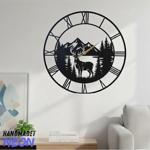 May include: Black metal wall clock with a nature scene featuring a deer, mountains, and trees. The clock has Roman numerals and gold-colored hands. The clock is mounted on a white wall.
