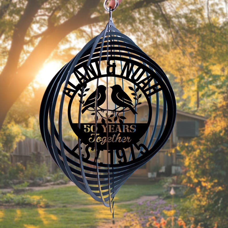 May include: Black metal wind spinner with a spiral design. The center features a circular design with two birds, the names "BLAN & NOAH", and the text "50 YEARS Together" and "Since 1973".