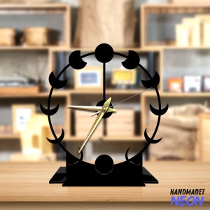 May include: Black metal clock with a moon phase design. The clock has gold hands and a black base. The clock is on a wooden surface.