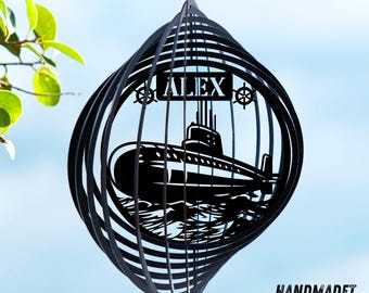 May include: A black metal wind spinner featuring a cutout design of a submarine on water with the name ALEX and two ship wheels. The circular structure consists of multiple concentric rings that create a three-dimensional spherical shape.