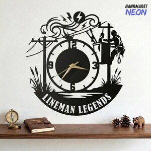 May include: Black metal wall clock featuring a lineman silhouette working on a power line, with the words "LINEMAN LEGENDS" at the bottom. The clock has gold-colored hands and the text "HANDMADET NEON" in the upper right corner.