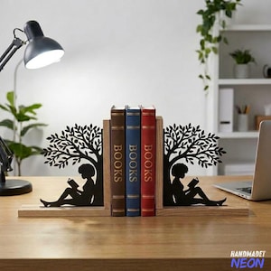 May include: Decorative black metal bookends featuring a silhouette of a person reading under a tree. The bookends hold three books with the word "BOOKS" on the spines. The bookends sit on a wooden base. The word "HANDMADET NEON" is in the bottom right corner.