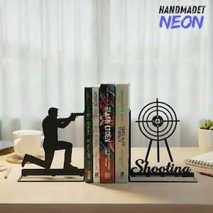May include: Black metal bookends featuring a silhouette of a person aiming a gun and a target with the word "Shooting". The bookends are holding several books. The text "HANDMADET NEON" is in the upper right corner.
