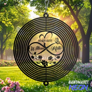 May include: Black metal wind spinner with a circular design. The centre features a heart, infinity symbol, date, butterfly, and names "William & Kate." The outer ring has concentric lines. The words "HANDMADET" and "NEON" are at the bottom.