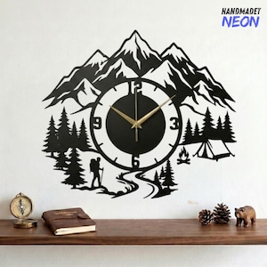 May include: Black metal wall clock with a mountain and forest design. The clock face is a circle with gold hands and numbers. The design includes a hiker, trees, a tent, and a campfire. The text "HANDMADET NEON" is in the upper right corner.