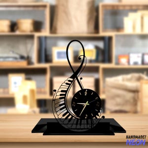 May include: Black metal clock shaped like a treble clef with a piano keyboard design. The clock face is black with gold hands and gold musical notes.