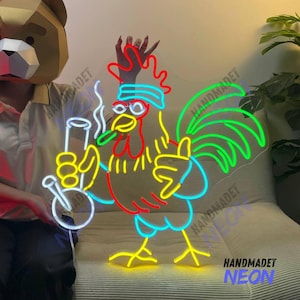 Puede incluir: Un letrero de neón que representa a un gallo de dibujos animados sosteniendo una pipa de agua. El gallo es rojo, amarillo y azul, con una cola verde. La pipa de agua es blanca y transparente. El letrero está hecho a mano y dice "HANDMADET NEON" en la parte inferior.