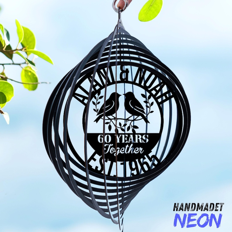Pode incluir: Moinho de vento de metal preto com design em espiral. O centro apresenta os nomes "ALANA & NOAH", dois p&aacute;ssaros e o texto "60 YEARS Together EST 1963". O canto inferior direito tem o texto "HANDMADET NEON".