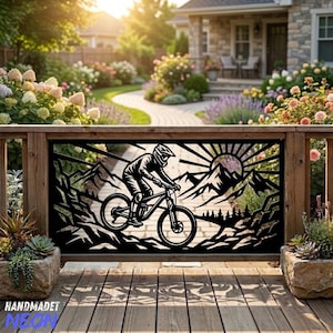 May include: A black metal decorative panel featuring a laser-cut silhouette of a person riding a mountain bike down a rocky trail. The design includes jagged mountain peaks, a sunburst pattern in the background, and a forest of pine trees.