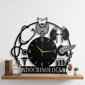May include: Black metal wall clock with a medical theme, featuring a clock face, stethoscope, and anatomical illustrations of the thyroid, kidneys, and pancreas. The word "ENDOCRINOLOGIST" is displayed below the clock.
