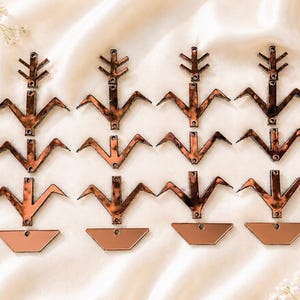 May include: A collection of six identical brown tortoiseshell patterned acrylic plant-shaped charms arranged in three rows. Each charm features a vertical stem with branches and a small trapezoidal base, all with small circular holes for attachment.