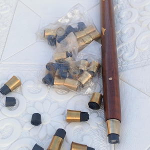 May include: A dark brown wooden walking cane with brass detailing and spare tips. The cane has gold-coloured metal accents. Several replacement tips are scattered around the cane, some in a plastic bag.