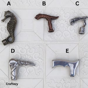 May include: A collection of decorative cane handles in various designs. The handles include a seahorse, a lion, a serpent, and a modern, curved design. The seahorse handle is bronze, while the others are silver or copper-toned.