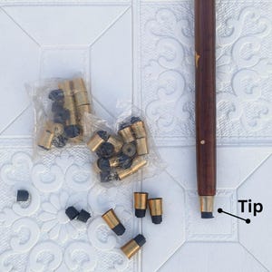 May include: A wooden walking cane with a dark brown finish and gold star accents. The image also shows replacement tips and ferrules in gold and black, packaged in clear plastic.