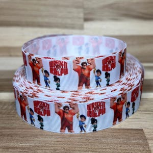May include: A white grosgrain ribbon featuring a repeating pattern of the Wreck-It Ralph logo in red text, alongside illustrations of the characters Ralph, Fix-It Felix Jr., and Vanellope von Schweetz, arranged in two stacked rolls.