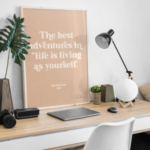 Może przedstawiać: Wydruk w ramie z brzoskwiniowym tłem i białym tekstem, kt&oacute;ry brzmi "The best adventures in life is living as yourself." Tekst jest w retro stylu czcionki. Na dole wydruku znajduje się tekst "Howl's Moving Castle 2004".