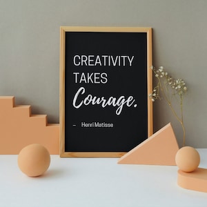 May include: A black framed chalkboard with the quote "Creativity takes courage." by Henri Matisse. The chalkboard is sitting on a white surface with peach-coloured geometric shapes.