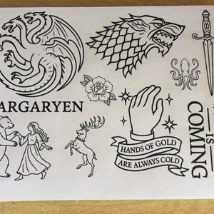 Puede incluir: Hoja de arte lineal en blanco y negro con varios símbolos y texto. Incluye un dragón de tres cabezas, una cabeza de lobo, una rosa, una mano con estrellas y las palabras "Targaryen" y "Winter is Coming."
