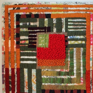 May include: A handcrafted textile art piece with a geometric design. The artwork features a central square of textured red fabric surrounded by green, brown, and white striped sections. Orange and red borders frame the piece, creating a vibrant, layered composition.