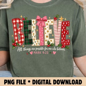 May include: An olive green t-shirt featuring the word BELIEVE in large, patterned letters with a pink bow on top. Below, the text reads All things are possible for one who believes. MARK 9:23, accented with holly berries and small pink hearts.